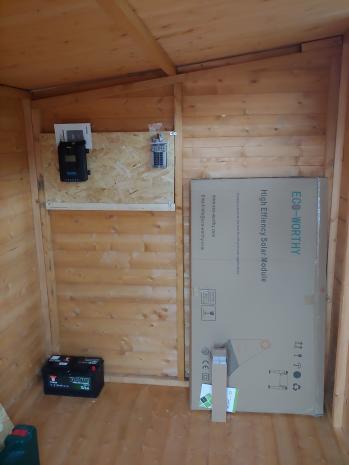 A shed with a board holding charge controller and fuse box mounted to one wall